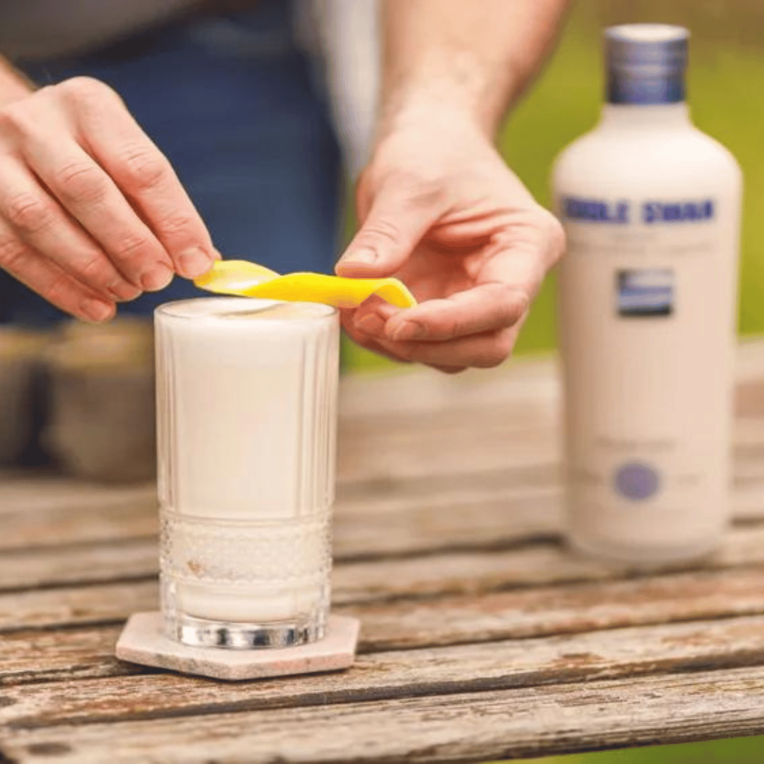 A glass of Coole Swan Irish Cream Liqueur being poured with a slice of lemon, alongside a bottle of the liqueur.